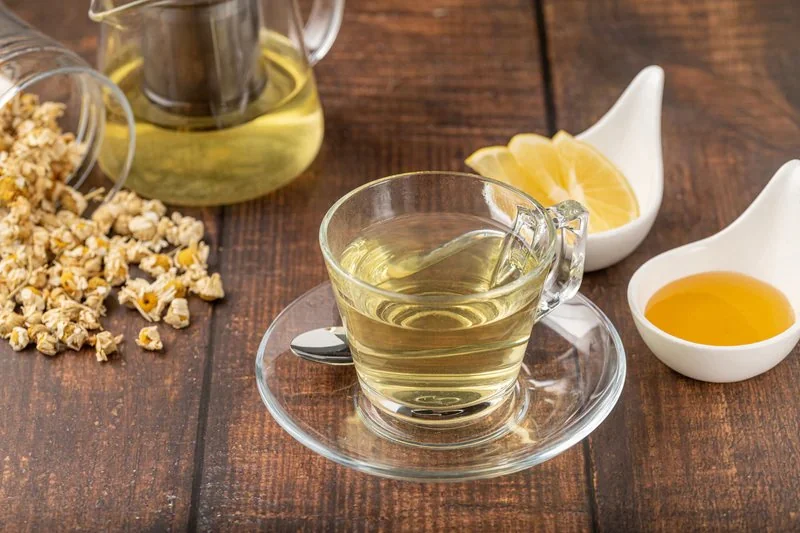 A glass cup of chamomile tea with dried chamomile flowers, lemon and honey