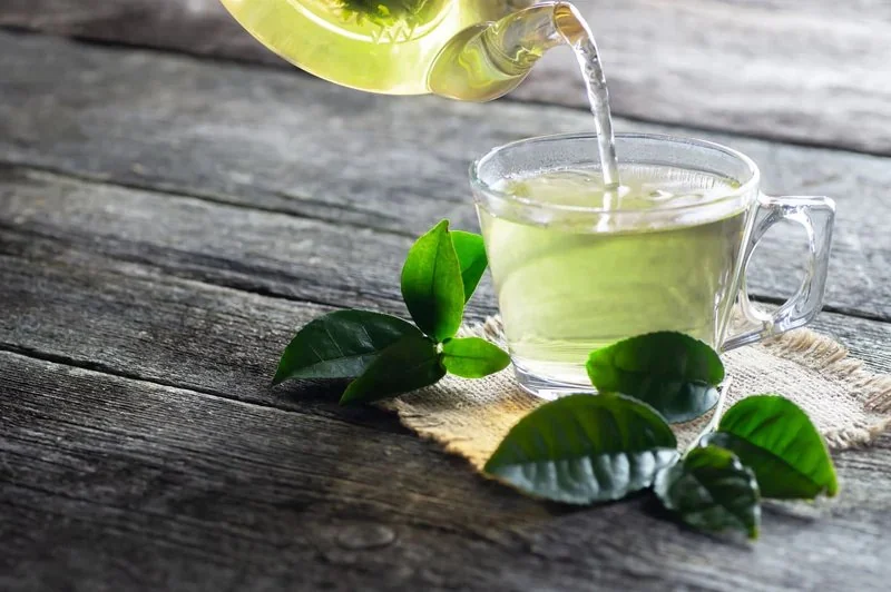 Green tea being poured from a glass teapot into a cup